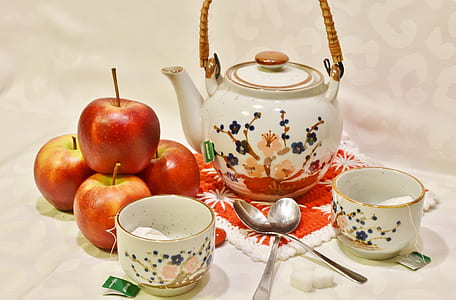 four red apples near white and multicolored ceramic teapot near two white ceramic teacups and two spoons thumbnail