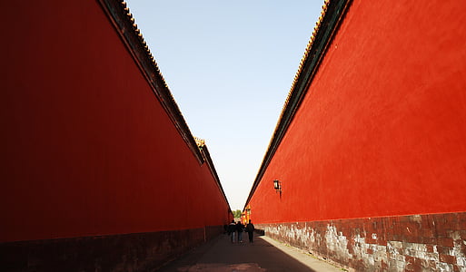 three people walking on concrete pathway between two red walls thumbnail
