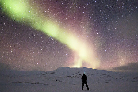 man standing on middle of snow-covered field with Aurora Borealis in background thumbnail