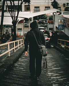 person wearing black hoodie walking beside rails thumbnail
