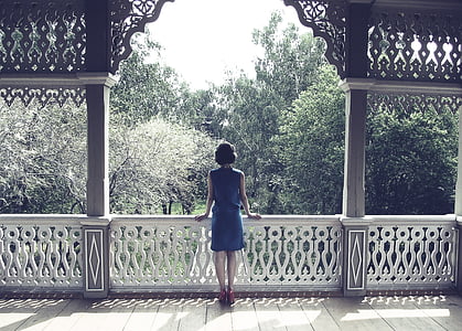 woman standing on balcony while facing trees thumbnail