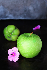 green apple beside pink flower on top of black surface thumbnail