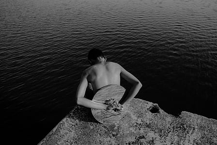 topless person on rock near body of water thumbnail
