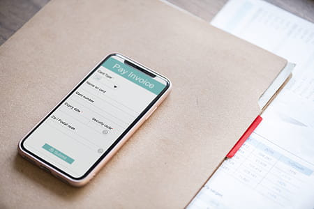 space gray iPhone X displaying pay invoice on top of brown folder thumbnail