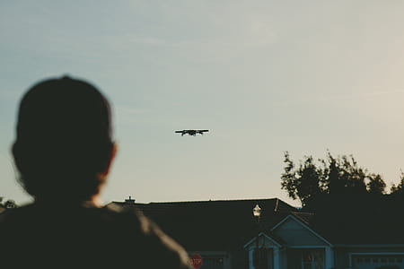 boy standing near brown house seeing flying airplane thumbnail