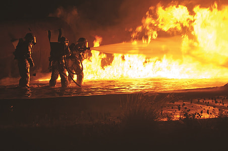 three fire fighters holding water hose in front of flames thumbnail