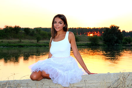 woman wearing white sleeveless dress sitting beside a lake at daytime thumbnail