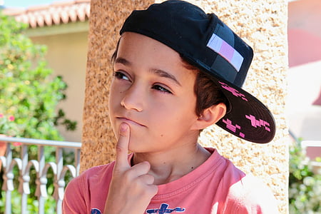 boy with left index finger on his chin beside post during day thumbnail