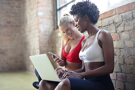 Two Young Women Wearing Red and White Sports Bras Using Laptop And Mobile Phone in Aerobic Dance Class thumbnail