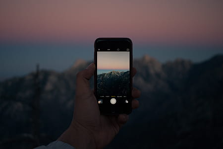 silhouette photo of a person holding smartphone taking a photo of cliff thumbnail