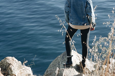 person stands on grey cliff near body of water during daytime thumbnail