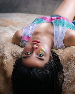 woman in white, blue, teal, and pink tie-dyed tank top laying on brown fur sheet close-up photography thumbnail