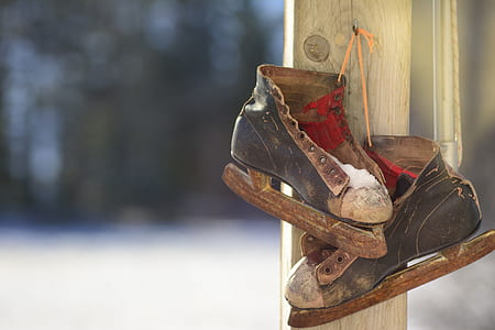 old black-and-brown ice skates hanging on gray wooden post during daytime thumbnail