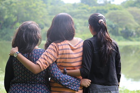 three women holding each other facing body of water thumbnail