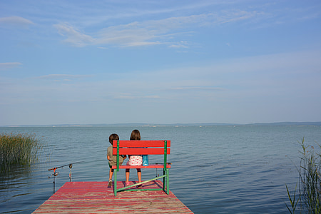 two children sitting on red and green wooden bench on bridge thumbnail