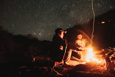 two persons sitting near bonfire under starry night thumbnail