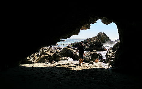person standing in front of cave near body of water thumbnail