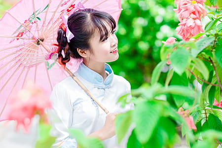 woman holding umbrella while standing near pink petaled flower during daytime thumbnail