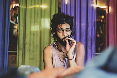 man smoking sitting near green and purple curtain thumbnail