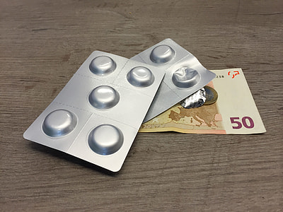 two gray blister packs on top of 50 Euro banknote on brown wooden surface thumbnail