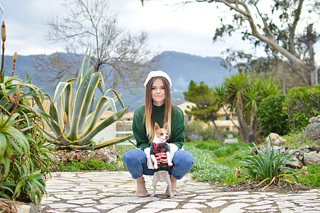 woman holding white chihuahua on white ceramic tiles near green plants thumbnail