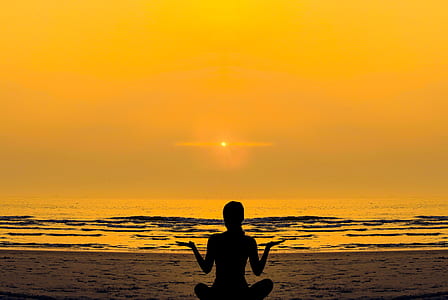 silhouette of woman meditating near body of water during sunset thumbnail