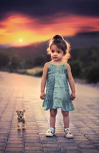 toddler girl's in green spaghetti strap dress and pair of blue-and-white low-top sneakers standing beside lon cab on grey concrete road thumbnail