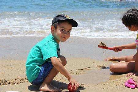 smiling boy wearing teal shirt playing on beach sand thumbnail
