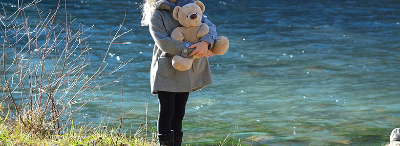 person hugging brown bear plush toy near body of water during daytime thumbnail