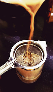 brown liquid filtered by stainless steel strainer to clear drinking glass thumbnail