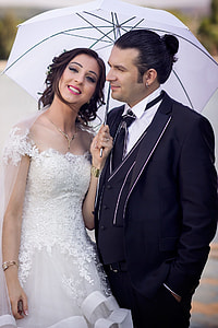 woman in laced white wedding dress standing while holding white umbrella beside man in black suit jacket thumbnail