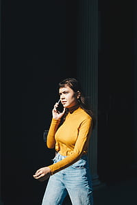 woman in yellow turtleneck long-sleeved shirt and blue jeans holding smartphone thumbnail