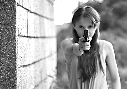 photo of woman wearing sleeveless top pointing gun near concrete wall thumbnail