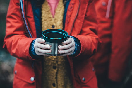 person in red zip-up jacket holding silver stainless steel cup filled with coffee thumbnail