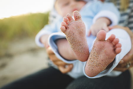 selective focus photo of baby's feet with sand carried by person thumbnail