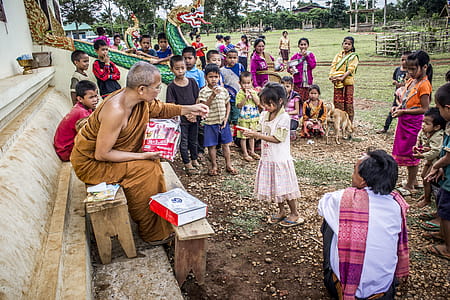 Monk in Front of Children Near Brown Concrete Building thumbnail