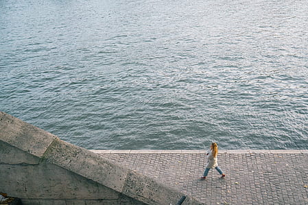 woman walking near body of water during daytime thumbnail