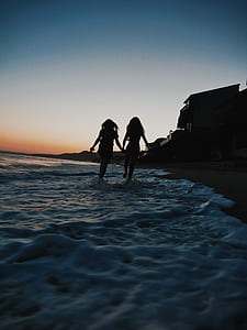 silhouette photo of two women walking on shoreline thumbnail