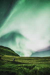 two people standing on green grass under green and blue sky thumbnail