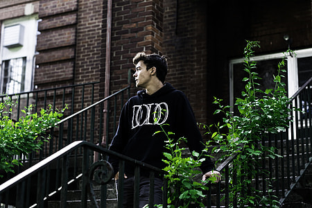 man wearing black hoodie standing beside brown metal rails thumbnail
