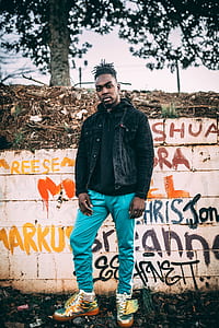 shallow focus photography of man standing in front of wall with graffiti thumbnail
