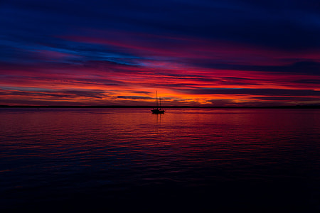 silhouette of water boat on calm body of water during golden hour in skyline photo thumbnail