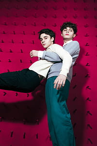 two man in sweatshirts standing near red wall photography thumbnail