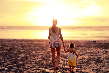 woman holding hand of girl while walking on sand field thumbnail