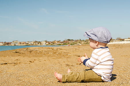 baby sitting on sand facing seashore thumbnail