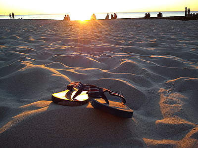 pair of flip-flops on beach sand during sunset thumbnail