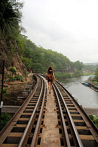 woman waling on brown metal rail road during daytime thumbnail