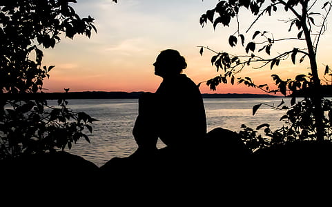 silhouette photography of person sitting on rock with view of sea thumbnail