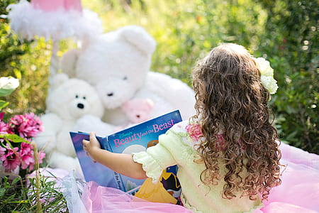 toddler girl seats in front of white teddy bears holding book thumbnail