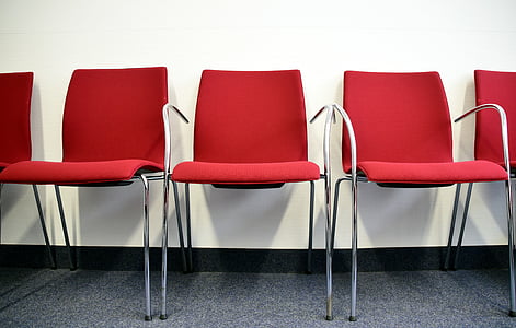 five gray metal framed armchairs with red pad behind white wall thumbnail